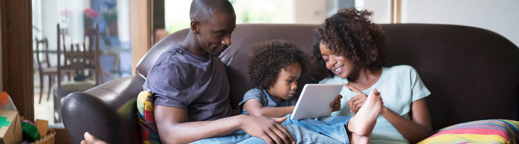 A family sits on a couch looking at a tablet